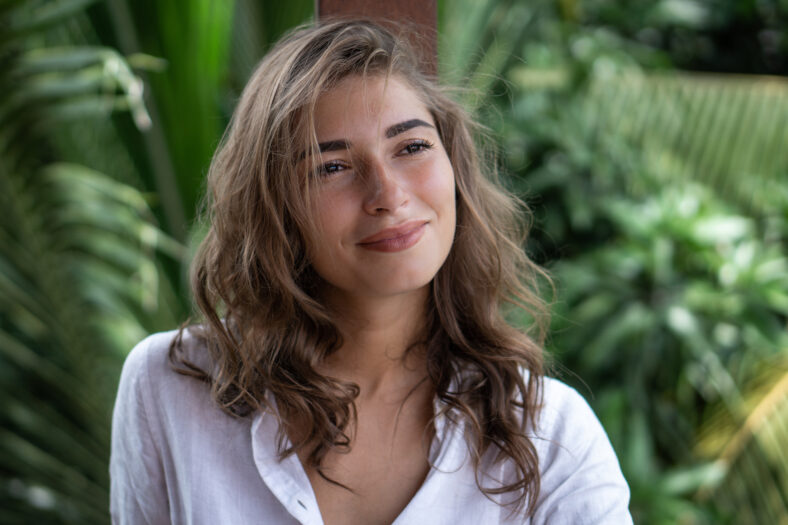 Retrato de joven hermosa mujer cerca de camisa blanca en balcón de bungalow tropical con palmeras vista en Bali