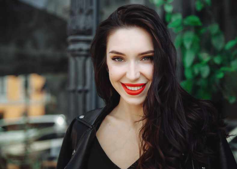 Amazing joyful pretty girl with long brunette hair wearing in leather jacket. Close up fashion portrait of pretty seductive young woman. Red lips, wavy hairstyle. Model smiling and looking at camera.