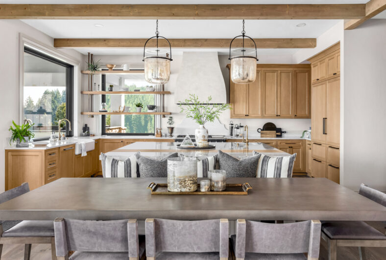 Gorgeous kitchen and dining table in new luxury home. Features pendant lights, hardwood cabinets, wood beams, and large kitchen island.