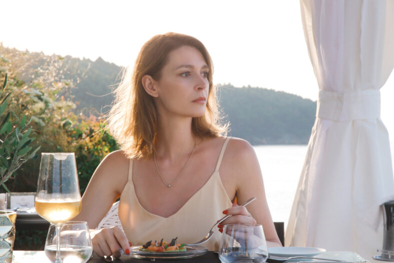 Young woman having dinner with a glass of wine at the beach restaurant