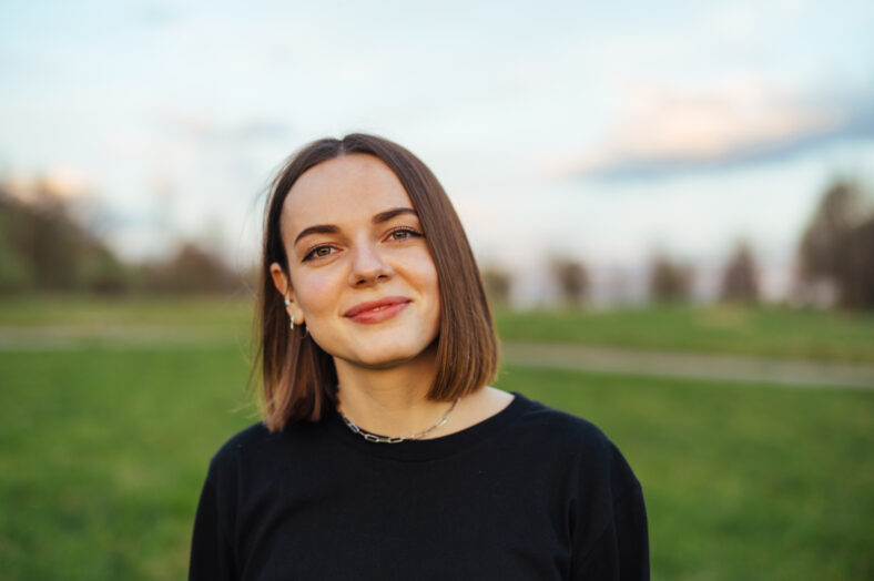 Close-up portrait of a smiling woman with a bob hairstyle in casual clothes in the evening at sunset on the background of the park, looking at the camera with a happy face