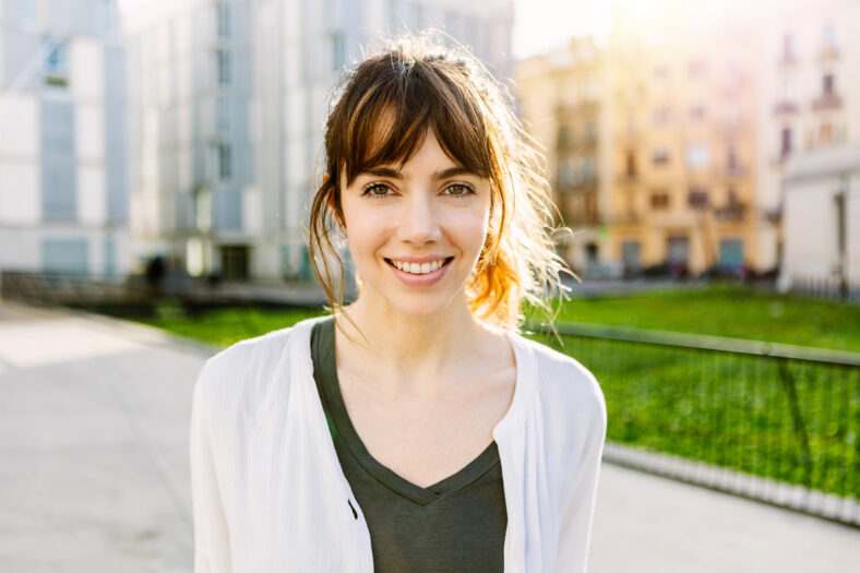 Outdoors portrait of beautiful young girl smile at camera over urban city background