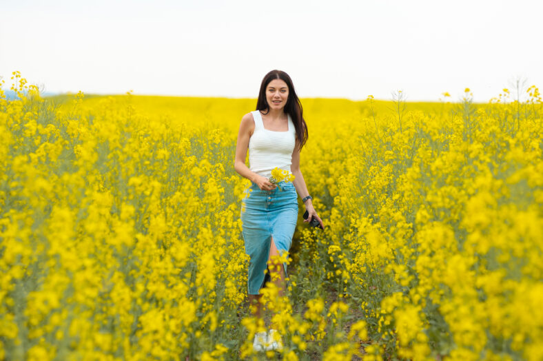 Happy beautiful woman walking on the field with yellow flowers
