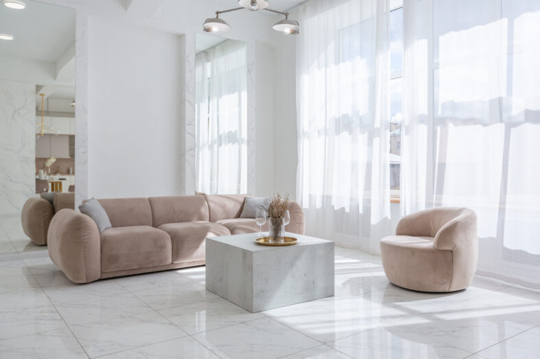 living room with soft beige furniture in a light luxury interior design of a modern apartment in a minimalist style with marble trim and huge windows. daylight inside.