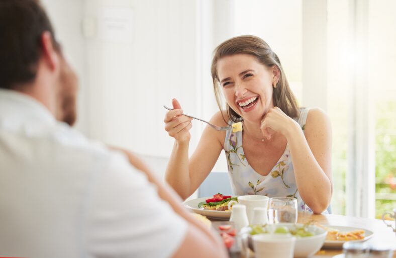 Couple, eating breakfast and home with talking, happy or food for health, wellness or diet in morning. Woman, man and comic laugh together for conversation, memory or relax on vacation in dining room.