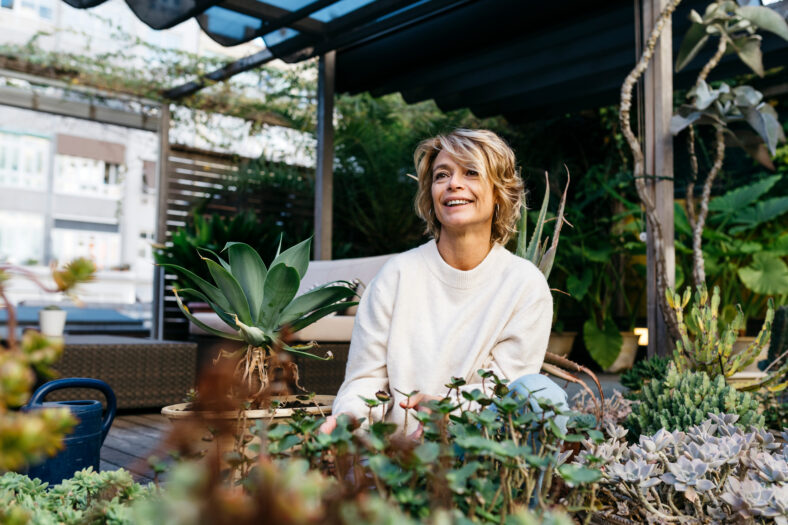 Smiling woman looking away amidst plant at rooftop garden