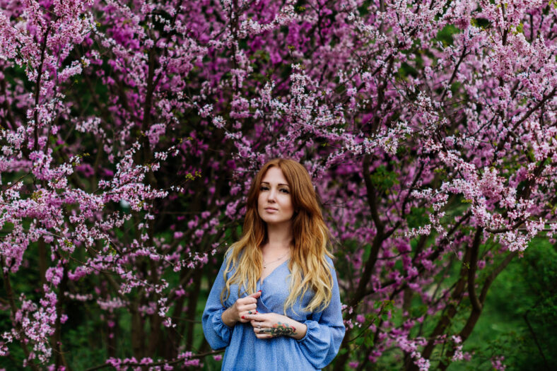 Beautiful smilling redhead woman in spring time blossom cherrytrees garden. Perfect time for a walk. Enjoy the spring and sunny day. Social media, beauty, blogger, vlogger.