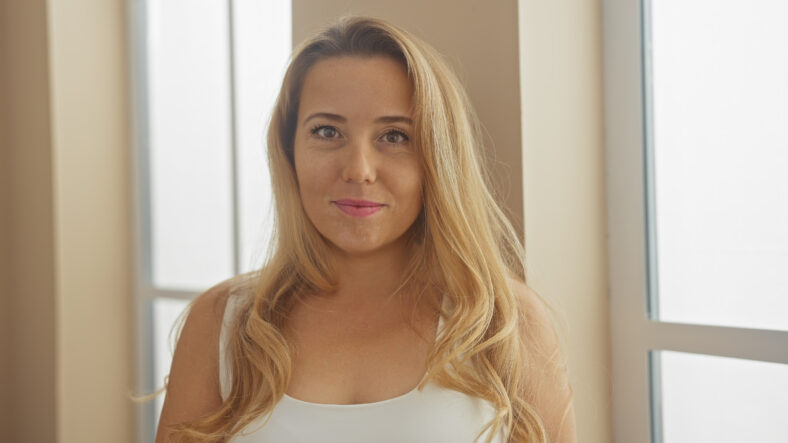 Portrait of a young, attractive, blonde caucasian woman in a bright indoor home setting.