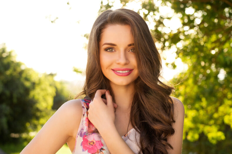 Hermosa chica sonriente que te mira contra el fondo de la primavera verde bokeh