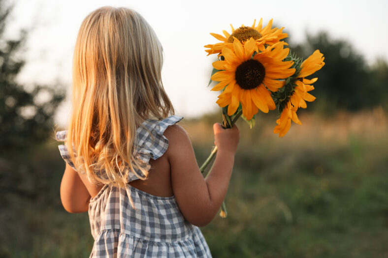 Little girl with sunflowers at meadow, back view. Child enjoying beautiful nature