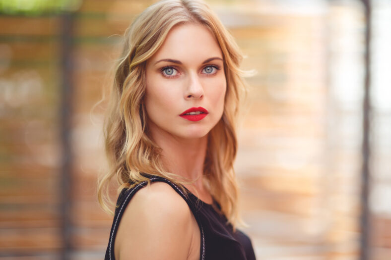 Closeup portrait of beautiful girl with curly blond hair and red lipstick on blurred background