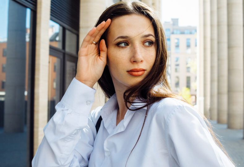 Fashionable brunette woman in the city. Young female model with long hair wears white shirt.