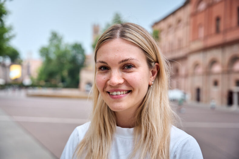Portrait of Caucasian woman looking at camera and smiling outdoors. Beautiful eastern European girl is happy and cute. She looks positive and attractive and confident laughing standing outside.