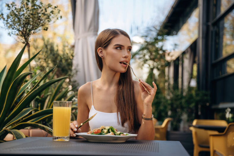 Delicious food. Beautiful young woman is outdoors of the restaurant by the table.