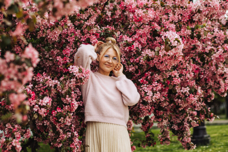 Young stylish woman wearing glasses surrounded by pink spring blossoms. Spring awakening and a new beginning. The concept of a healthy lifestyle, good vision, organic goods.