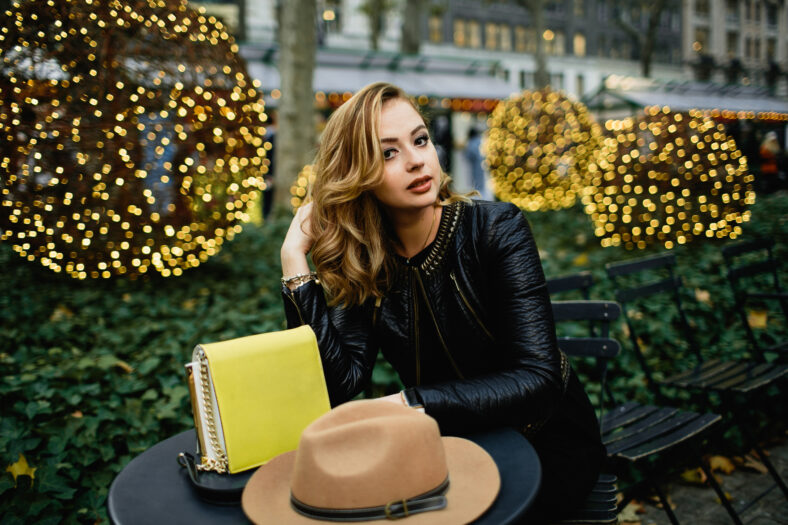 Gorgeous blonde woman sits at black round table before green bushes outside
