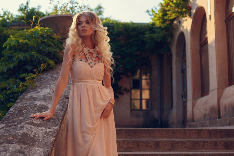 Young beautiful woman in long pink evening dress walking path in park. Fashion style portrait of gorgeous beautiful girl outdoors