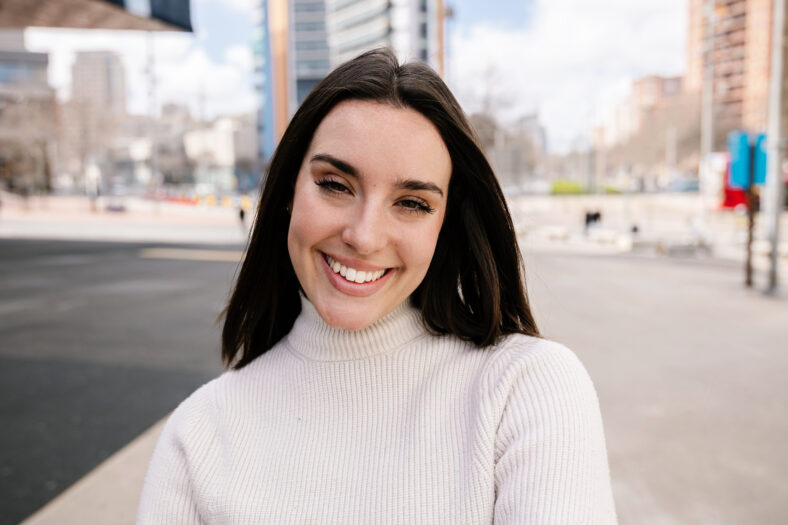 Portrait of young happy pretty woman smile at camera outside. Millennial cheerful girl showing toothy smile standing at city street