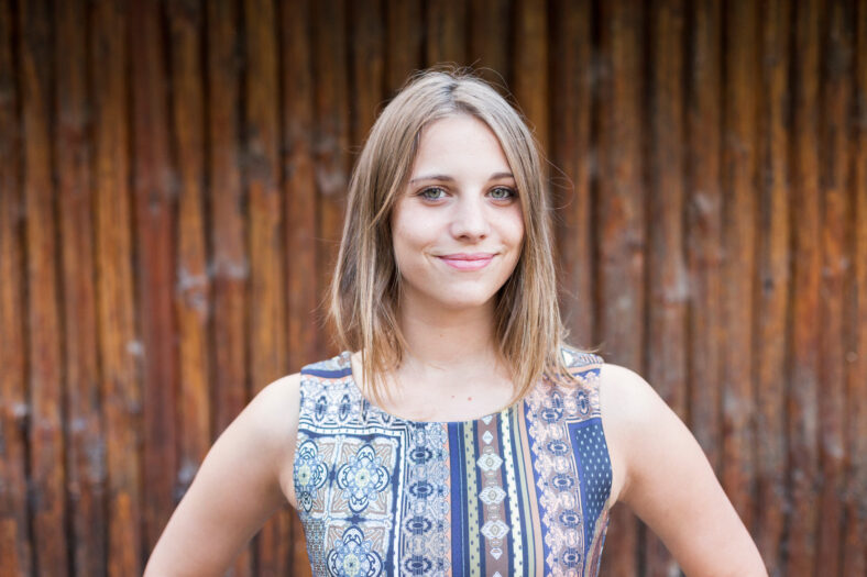 outdoors portrait of a beautiful young woman looking at the camera and smiling. Wood background. Beauty and lifestyle