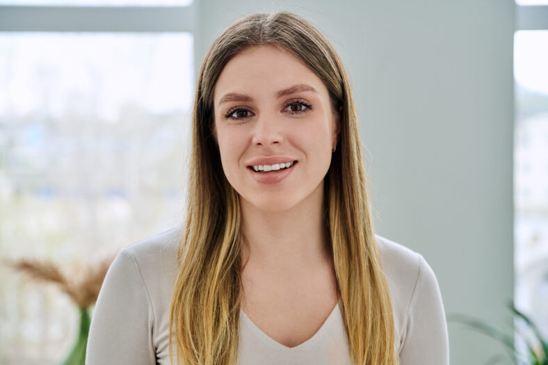 Headshot portrait of confident successful young woman posing in home. Smiling happy beautiful 20s female with blonde long hair looking at camera. Beauty, health, lifestyle, youth concept