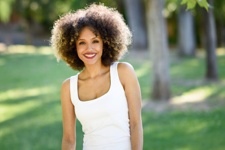 Young black woman with afro hairstyle smiling in urban park. Mixed girl wearing casual clothes.