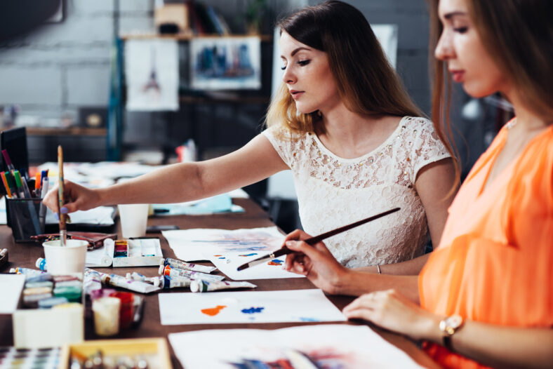 Two adult female students working on their paintings studying at art school.