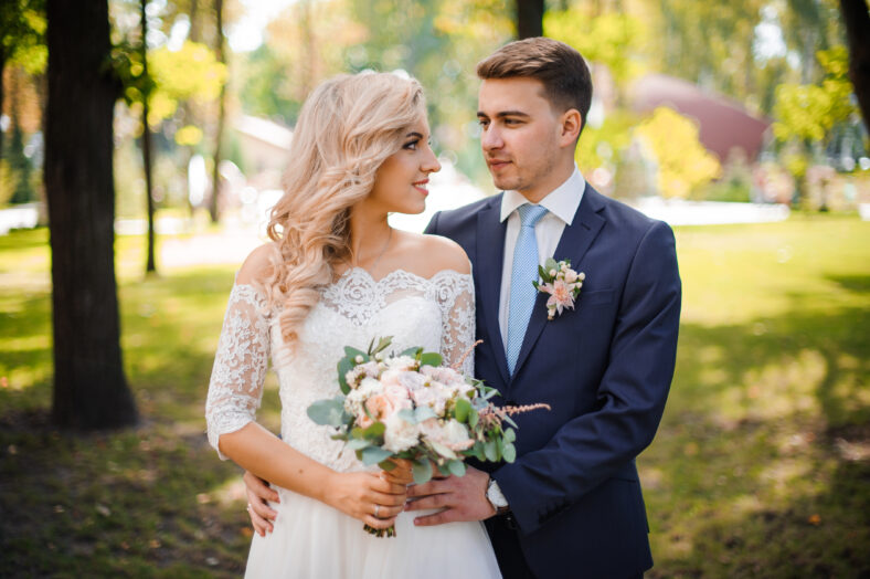 Portrait of a young bridegroom embracing a lovely blonde bride holding a beautiful bouquet of flowers