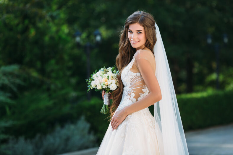 Amazing bride in beautiful white wedding dress hold bouquet of flowers in her hands. Concept of clothes and floristics.