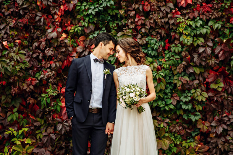 groom and bride posing in front of old brick wall with ivy