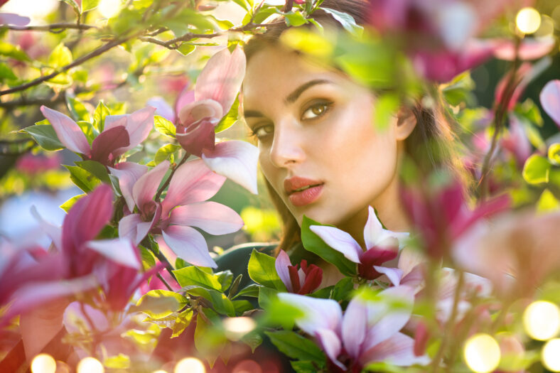Blooming magnolia trees. Beauty young woman touching and smelling spring magnolia flowers. Happy beautiful girl enjoying nature