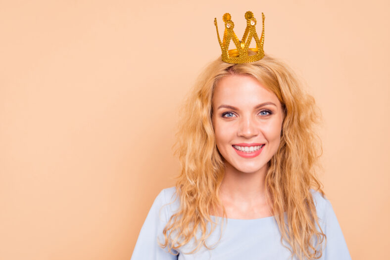 Portrait of attractive beautiful curly-haired cheerful blonde caucasian young girl wearing golden crown on head. Copy space. Isolated over grey background