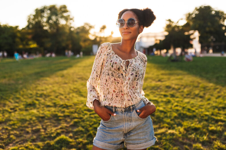 Young beautiful african woman in sunglasses dreamily looking in camera spending time in city park