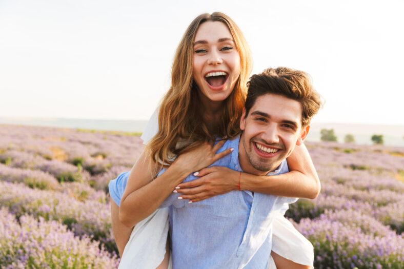Cheery young couple having fun at the lavender field together, piggyback ride