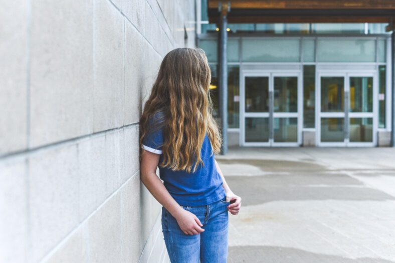 Teenage girl looking over her shoulder while leaning against a brick wall.