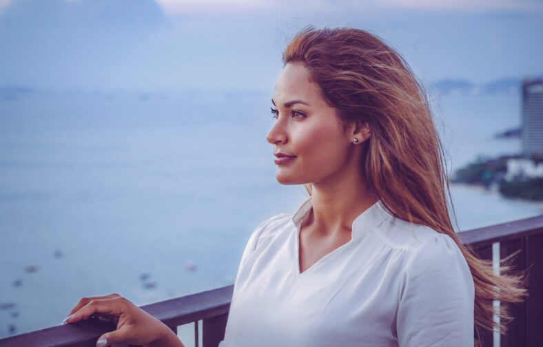 Portrait of young female model on the rooftop of a restaurant in Pattaya with ocean and city skyline in the back.