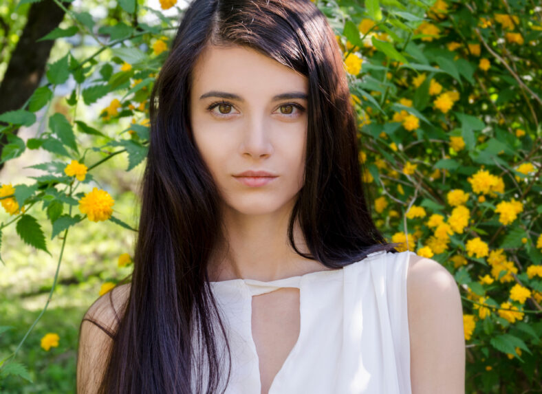 beautiful young girl with dark long hair, surrounded by yellow flowers, a warm spring day