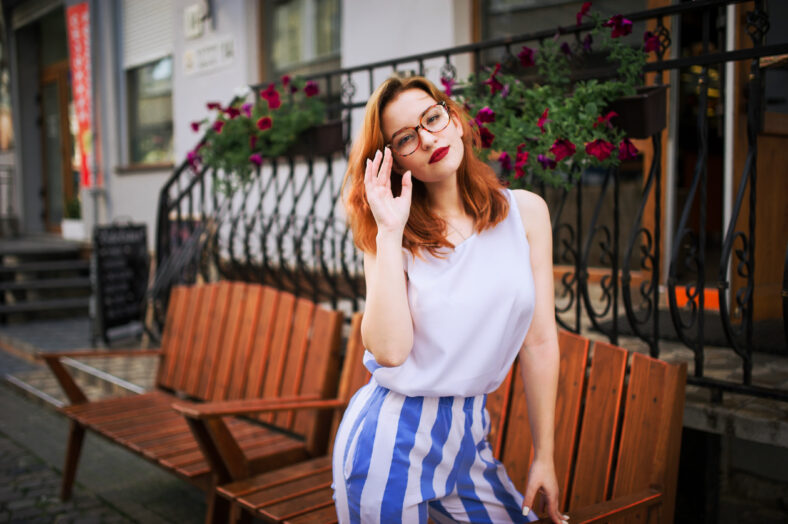 Attractive redhaired woman in eyeglasses posing at street of spring city.