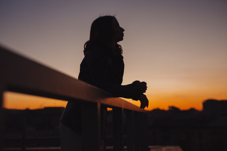 Silhouette of woman thinks and dreams about future at sunset in city