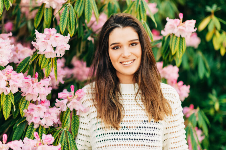 Outdoor portrait of beautiful young woman white knitted pullover, posing in spring garden