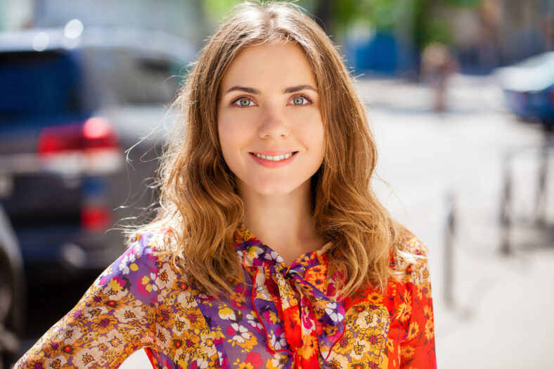 Portrait close up of young beautiful happy blonde woman in red dress, summer street outdoors