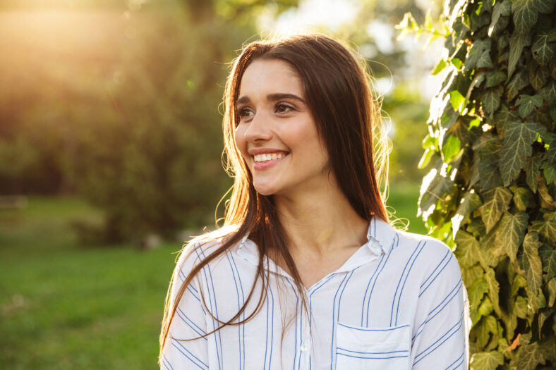 Photo of pretty young woman wearing striped shirt smiling and walking in green park on sunny day