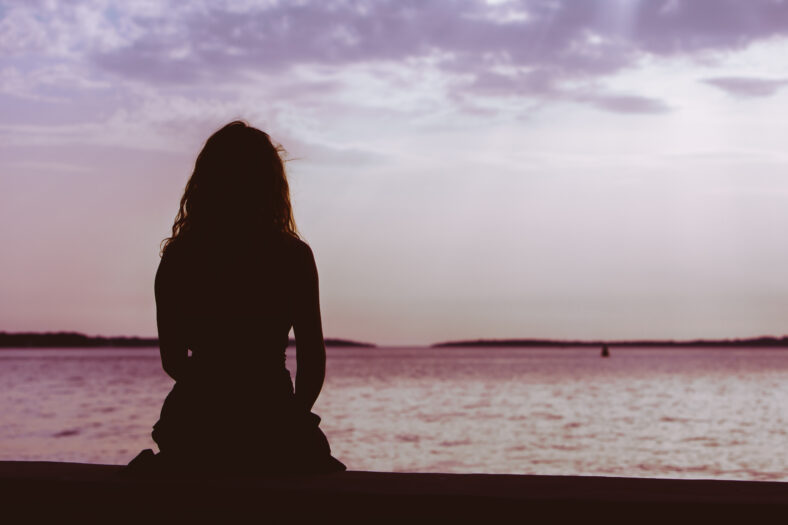 woman silhouette sitting on the beach looking at sunset over the sea. copy space