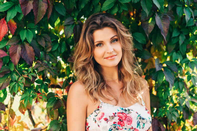 Outdoor portrait of beautiful woman wearing floral dress, posing in sunny garden