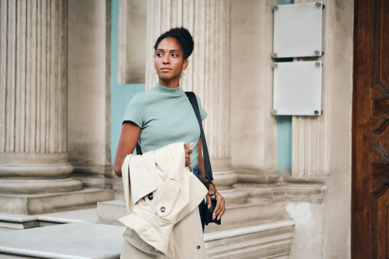 Beautiful confident African Amerian girl with trench coat in hand thoughtfully walking down the street