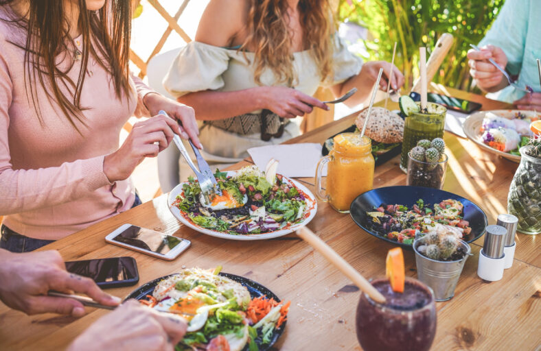 Hands view of young people eating brunch and drinking smoothies bowl with ecological straws in trendy bar restaurant - Healthy lifestyle, food trends concept - Focus on left woman hand, dish