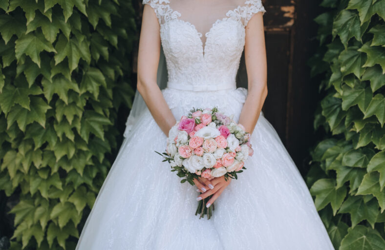 The bride in a white dress holds a wedding bouquet of roses in her hands. Closeup portrait of fresh flowers on nature, against a background of green foliage. Photography, concept.