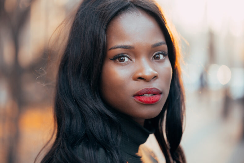 A beautiful young black African girl with a happy smile poses outdoors in the rays of the setting autumn sun. close-up.