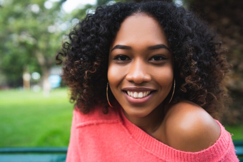 Portrait of young beautiful afro american woman sitting on bench in the park. Outdoors.