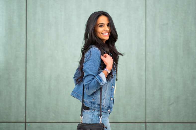 Side portrait smiling young latin woman with handbag by green wall