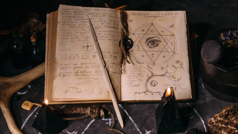 Open old book with magic spells, runes, black candles on witch table. Occult, esoteric, divination and wicca concept. Halloween vintage background